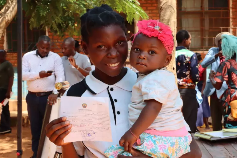 A mother holds her infant child and the birth registration certificate of her child.