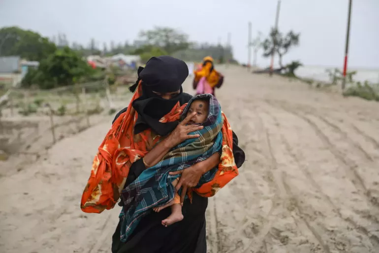 A mother holds her small child walking in muddy and flooded area.