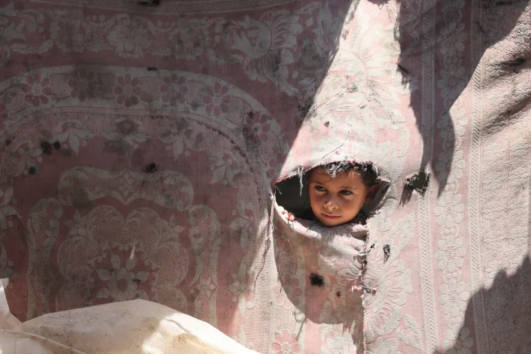 Jasser, a 7-year-old child from Gaza, looks out of one of the broken walls of a tent.