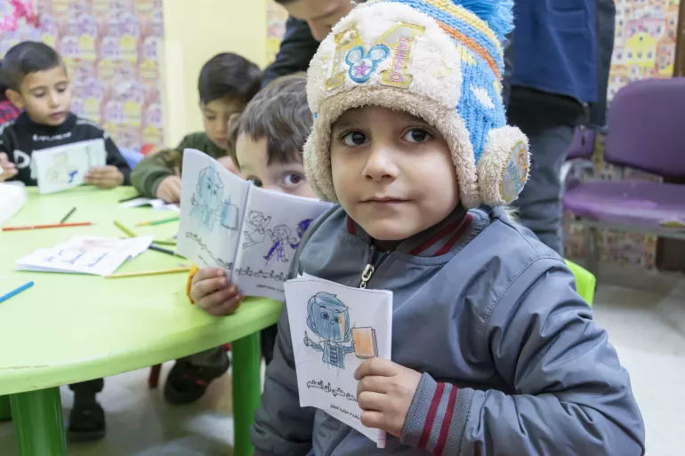 Un petit gar&ccedil;on est assis &agrave; un bureau dans une classe. Il tient dans sa main un dessin. 