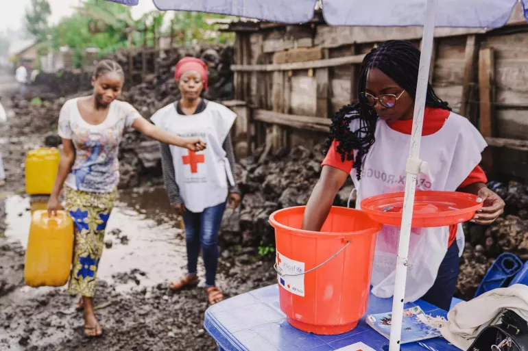 Three women add chlorine to water collected in buckets and jugs.