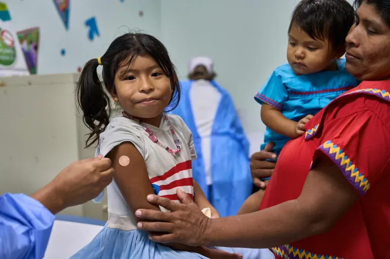 A young girl smiles and wears a band aid after getting vaccinated at a health care centre.