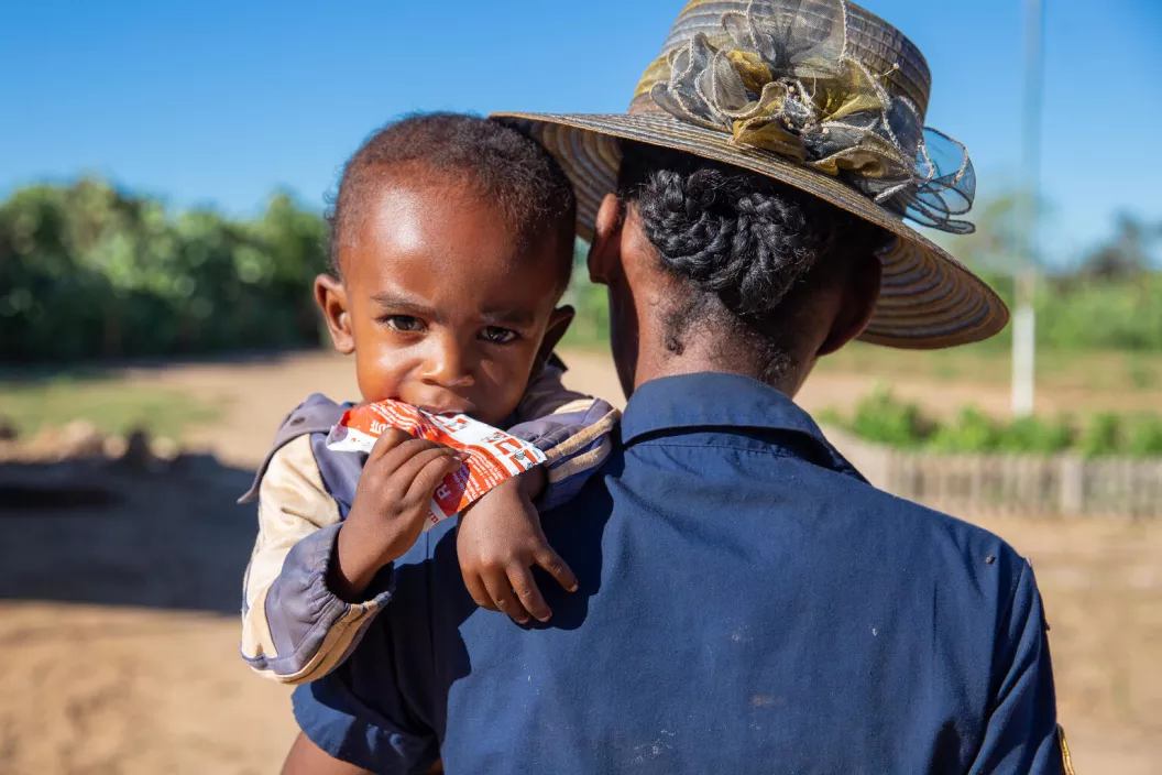 Madagascar. A woman carries her child as he eats ready-to-use therapeutic food.