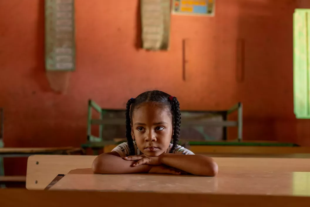 A six-year-old girl rests her chin and cross arms on a desk in an empty classroom in Kassala, Sudan.