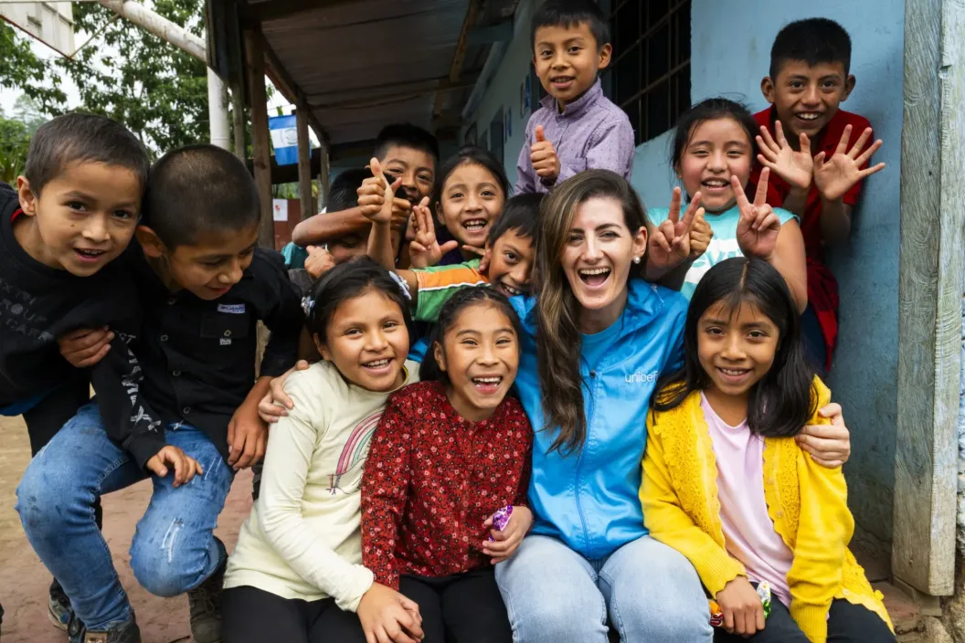 A UNICEF staff member smiles while posing with a group of children.