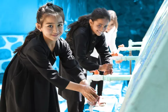 3 young girls standing in a line together washing their hands
