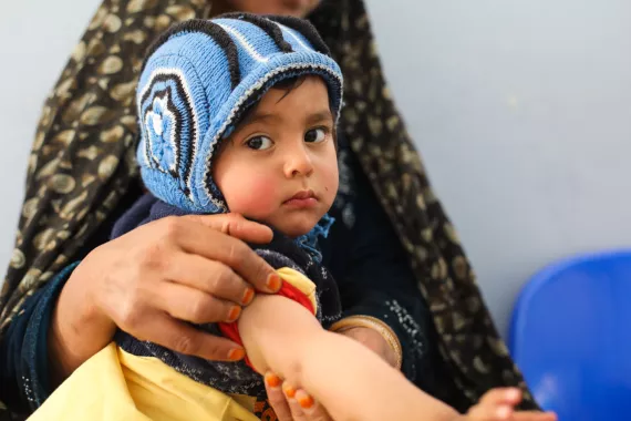 A young baby sits on their mother's lap with their sleeve rolled up