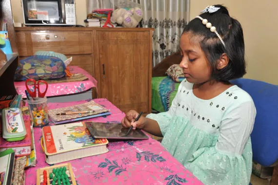 A young girl sitting at a desk in her bedroom using a computer tablet for schoolwork