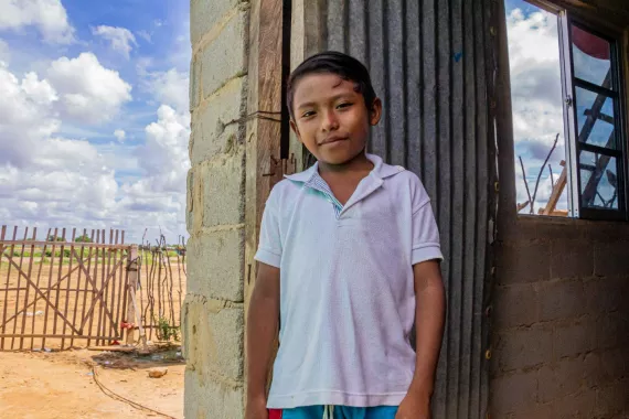 A young boy standing in fornt of a brick building with a corrugated metal door