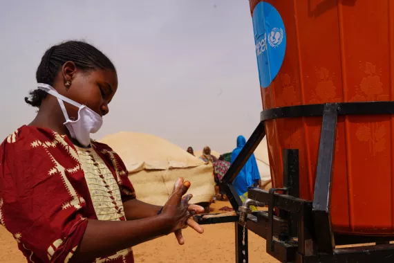 A teenage girl wearing a mask washing her hands at a UNICEF facility in a migrant camp in Niger