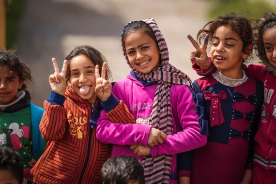 Iraq: In a camp for internally displaced, three girls dressed in bright colours happily pose for a photo.