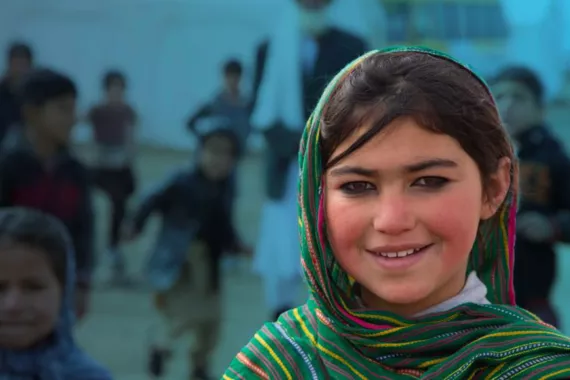A girl wearing a headscarf smiling with children in the background.