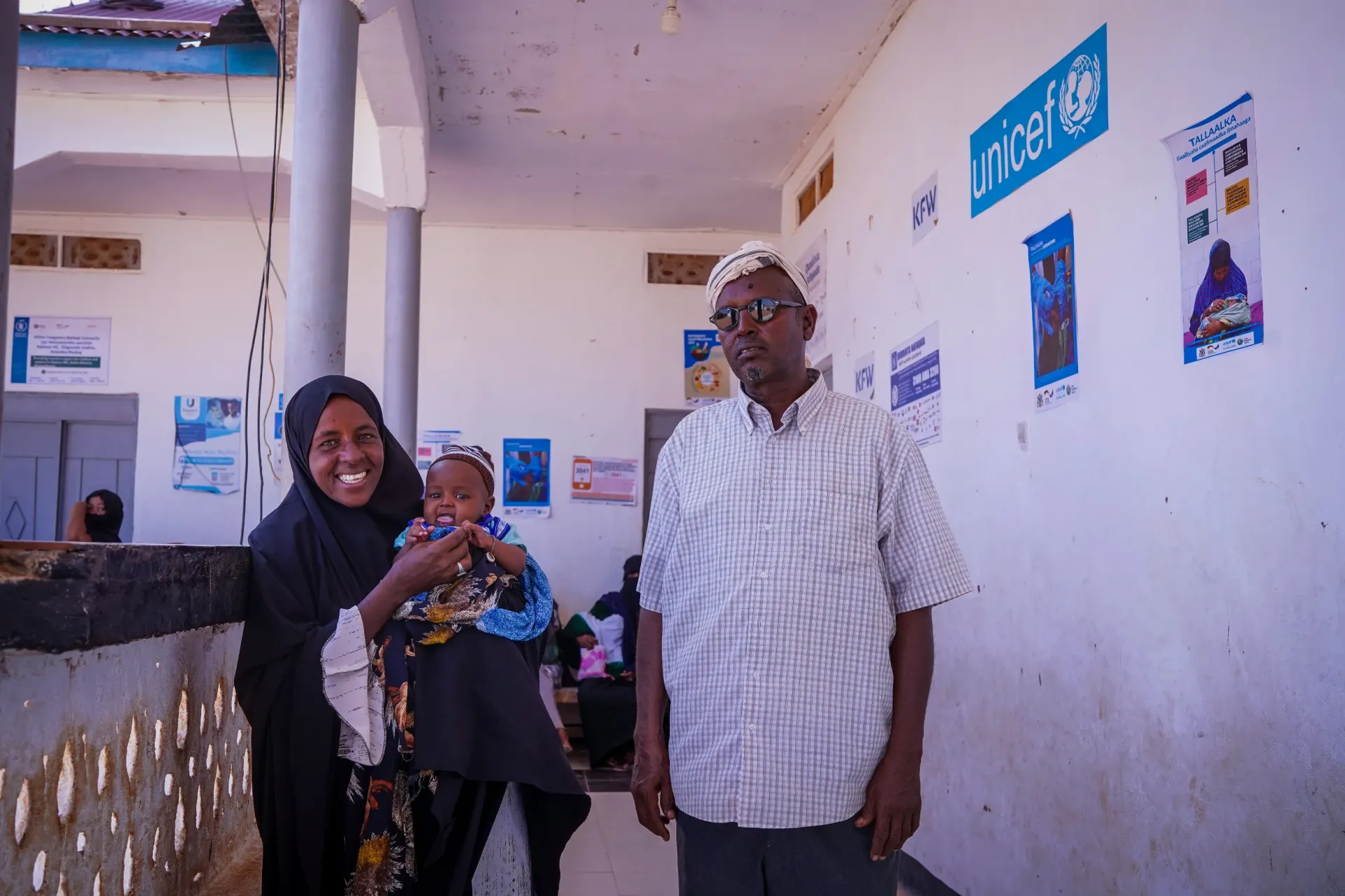 Mohamed stands with his wife and child outside the health centre, where they brought their child for a routine check-up together.