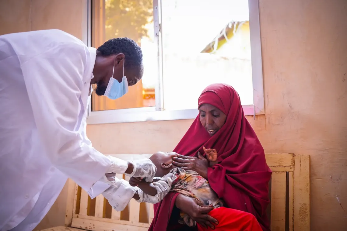 A health worker vaccinates Asho Abdullahi's youngest child at a health centre in Bardhere. After four of her children contracted measles during a recent outbreak, Asho is determined to protect her youngest through routine immunization.