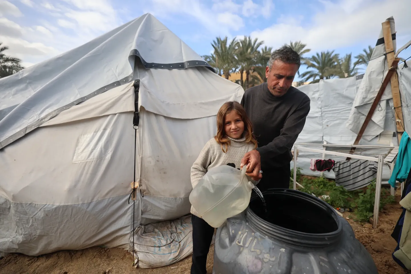 Fatima, 12, and her father pour clean water collected from a UNICEF-installed water tank nearby into their own family water tank for drinking and cooking.