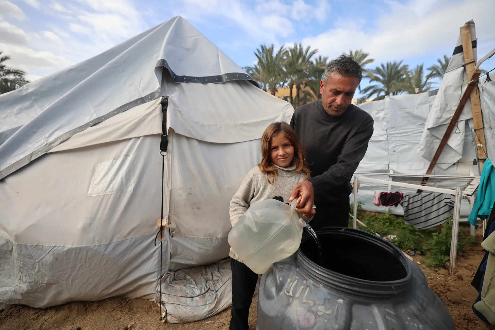 Fatima, 12, and her father pour clean water collected from a UNICEF-installed water tank nearby into their own family water tank for drinking and cooking.