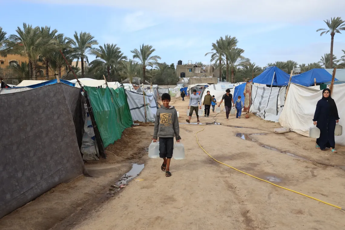 In a tent city in the Gaza Strip, an adolescent boy carries clean water from the UNICEF water point back to his shelter.