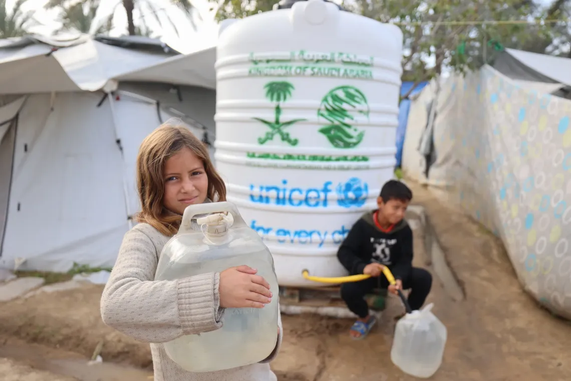 Fatima, 12, stands in front of one of the UNICEF-installed and serviced water tanks in Deir al-Balah near her family tent.&nbsp;