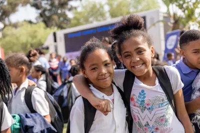 Two girls smile happily with the UNICEF truck and more children in the background.
