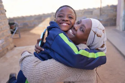 A mother and daughter hug each other tightly while smiling brightly.