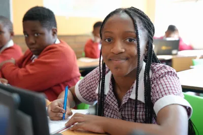 A girl sitting at a desk in class and wearing a school uniform looks up smiling