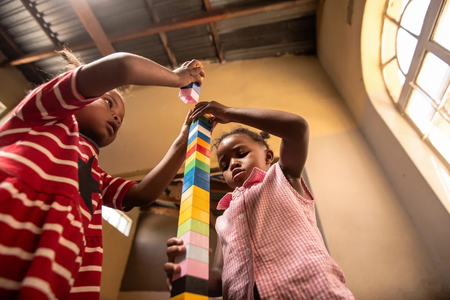 Two girls build a tall tower with colourful blocks.