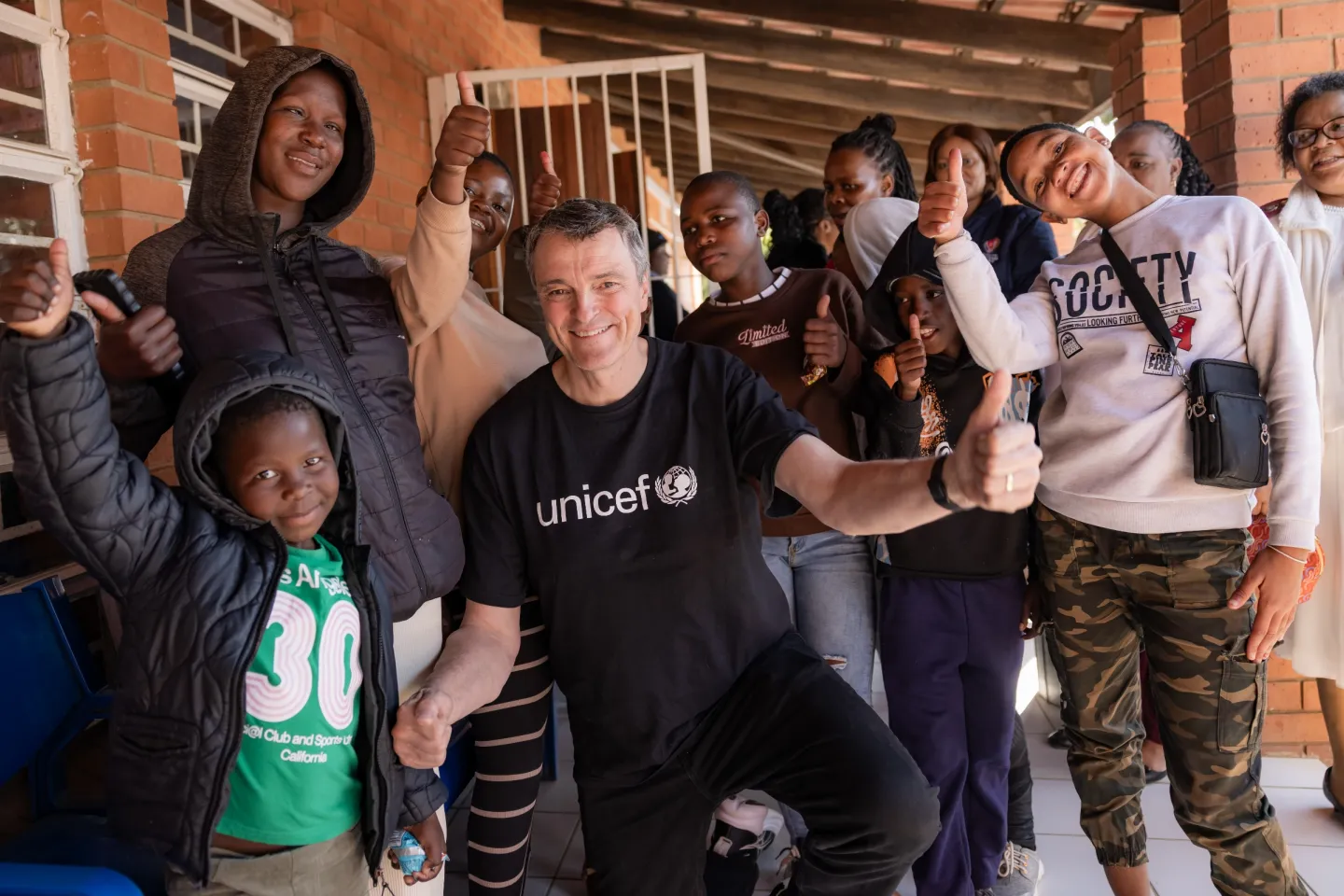 The UNICEF representative, wearing a black t-shirt with a UNICEF logo is surrounded by children and young people.