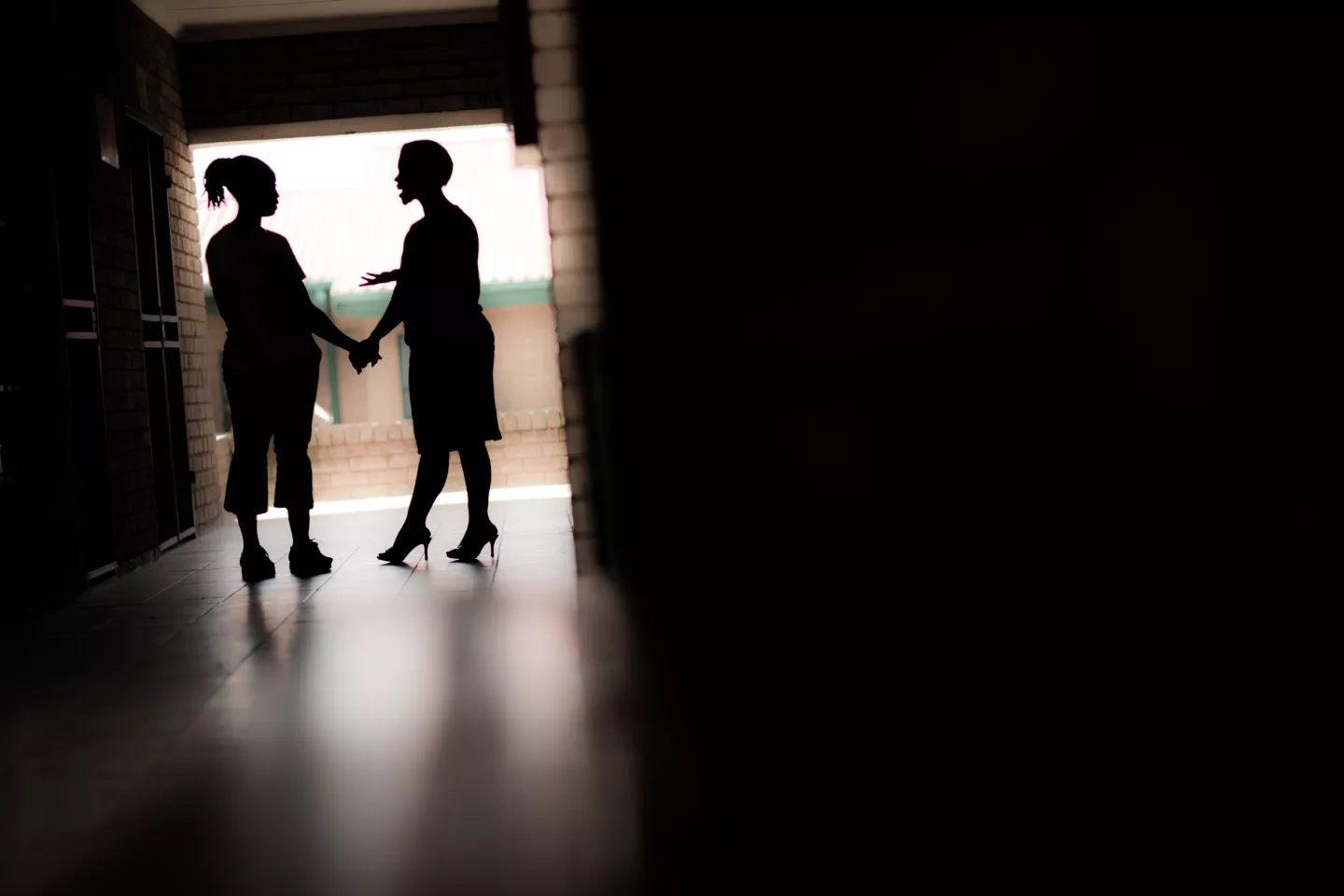 The silhouettes of a woman holding the hand of a teenage girl standing in a doorway