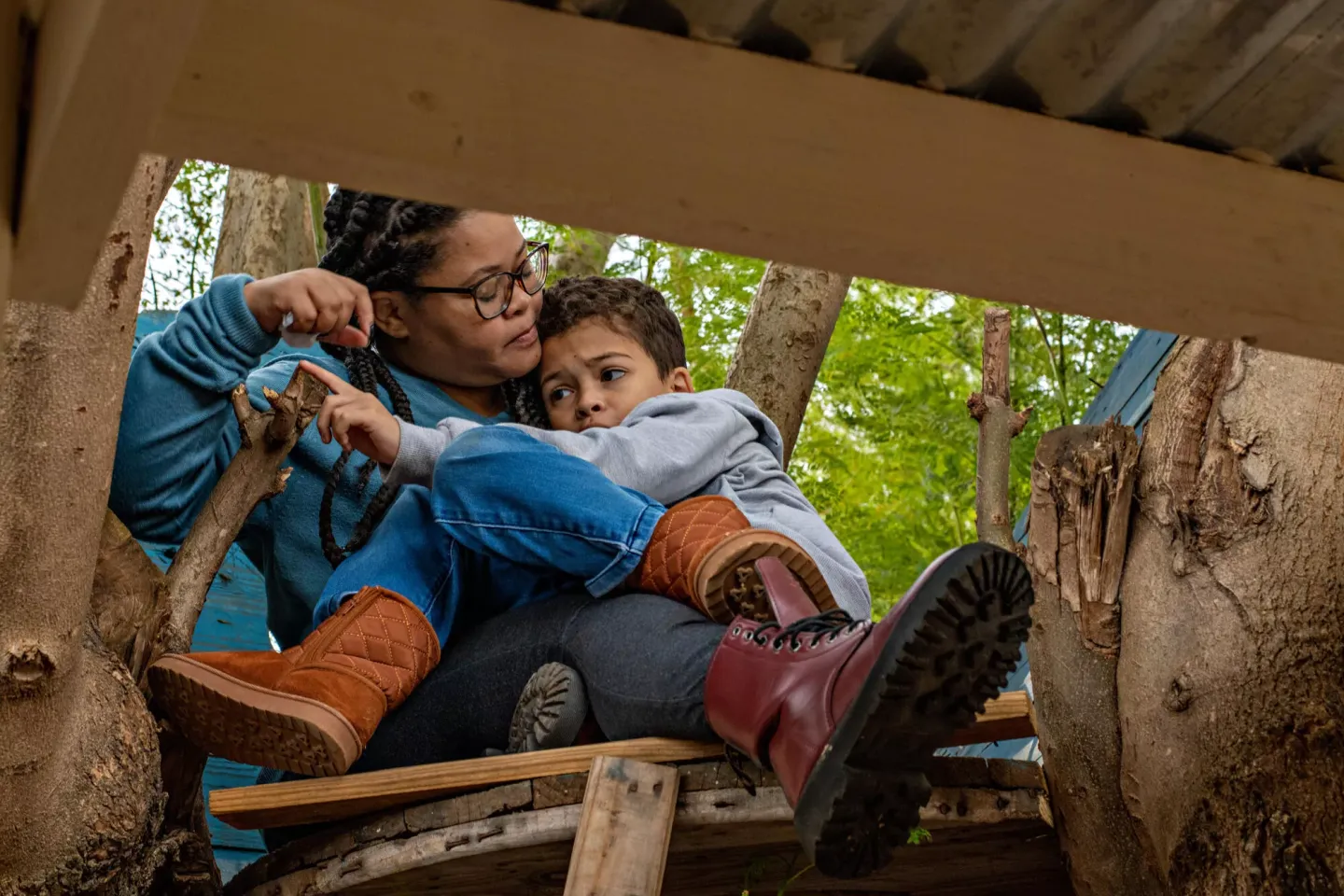 A boy frowning slightly, sits on his mother's lap with his arms wrapped around her neck, while she looks intently at his face.