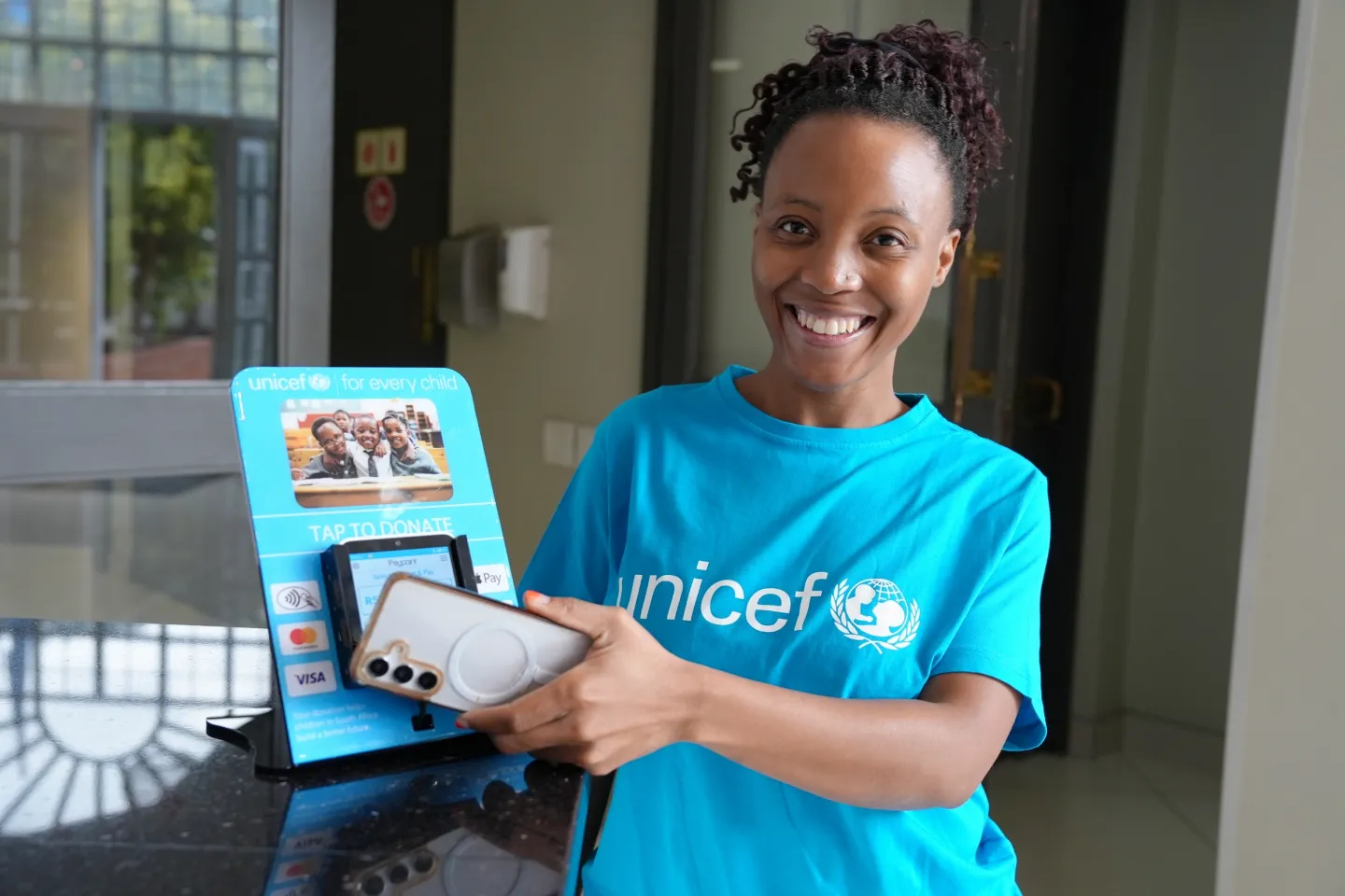 A woman wearing a UNICEF t-shirt, taps her phone on donate point of sales device.