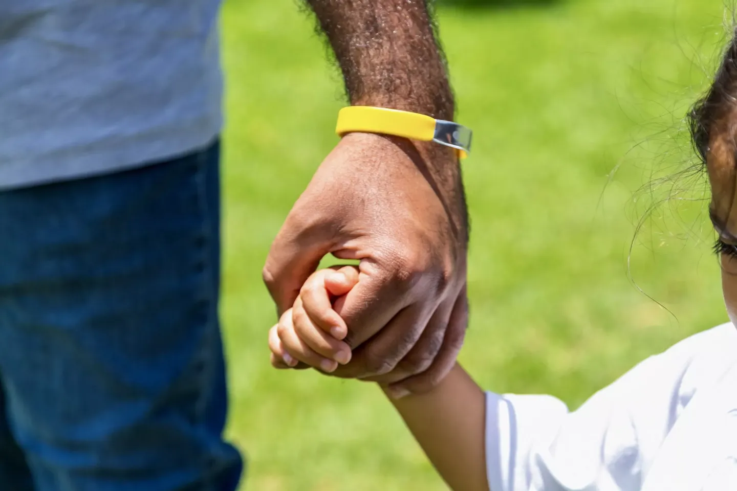The hand of a little girl holds on to her dad's hand with a yellow band around his wrist.