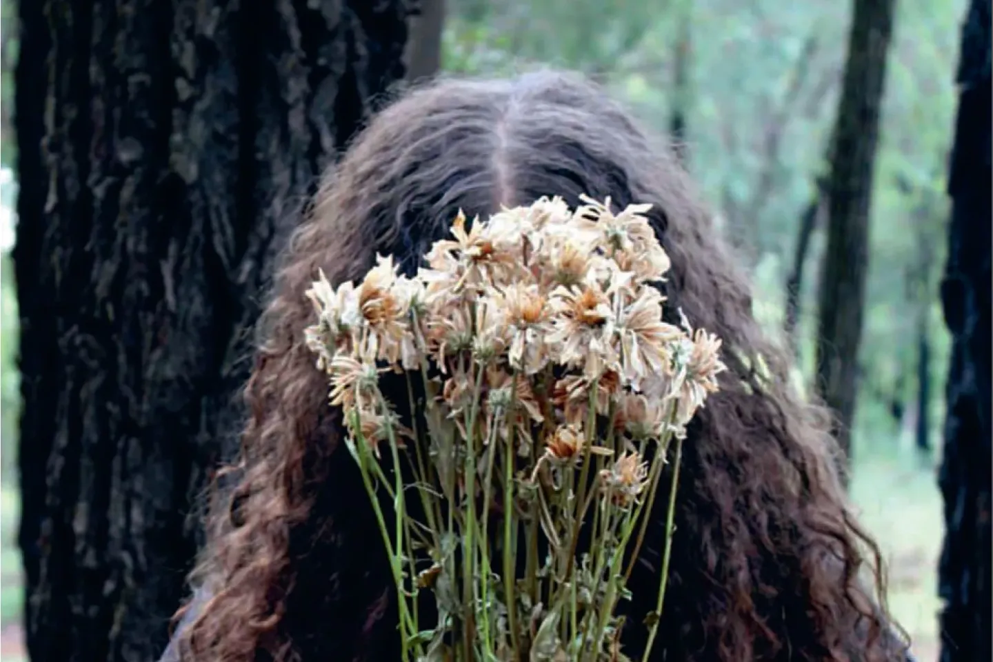 A girl's flowy dark hair is visible behind a bunch of wilted flowers.
