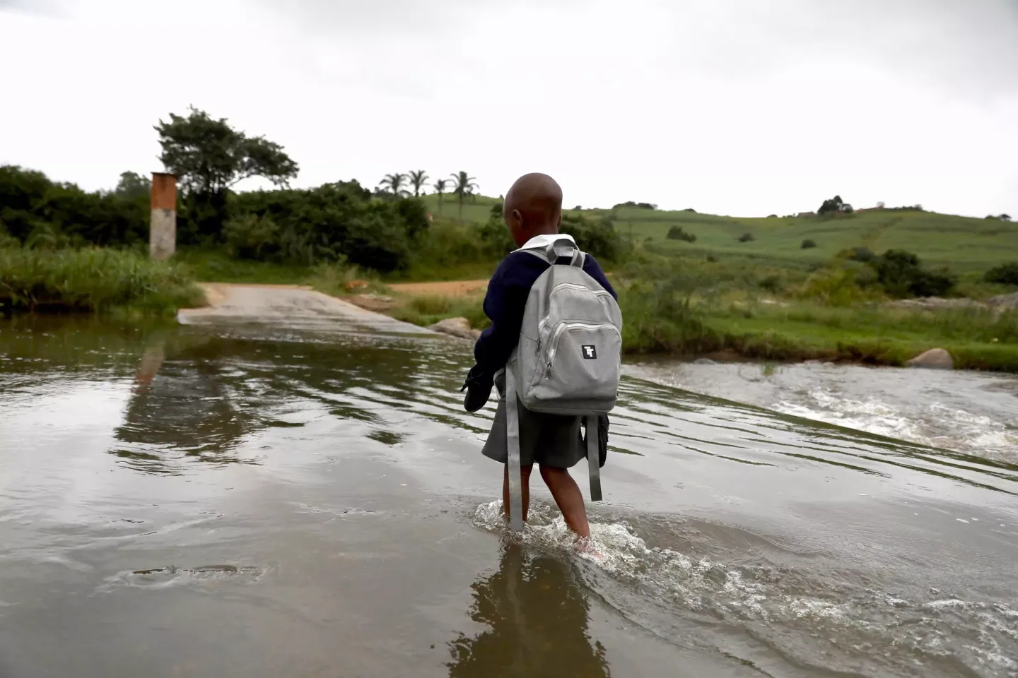A girl wearing a school uniform and with a rucksack on her back walks through floodwater.