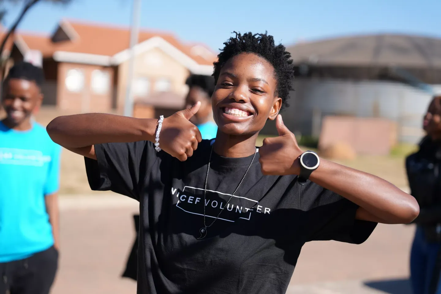 A UNICEF Volunteer wearing a black volunteer t-shirt smiles while holding up both thumbs.