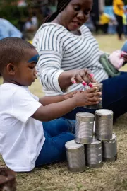 A little builds a tower with empty tin cans while his mother reaches out to assist him.