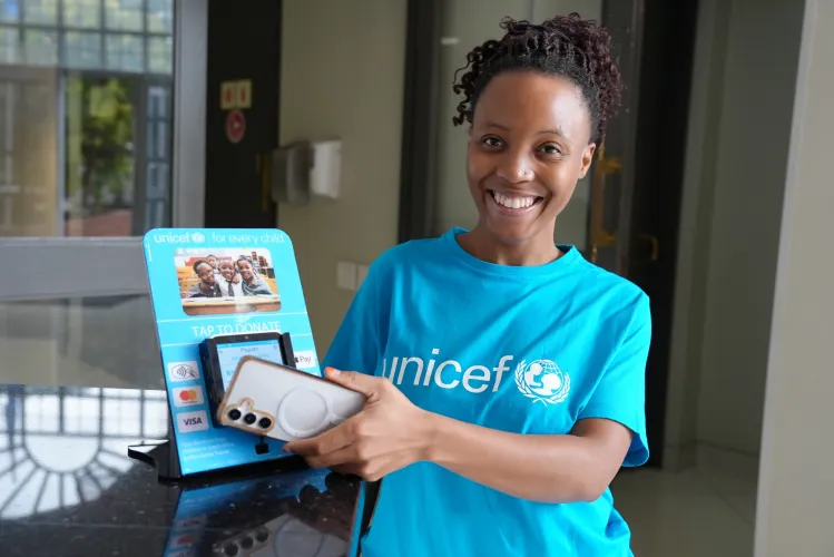 A woman wearing a UNICEF t-shirt, taps her phone on donate point of sales device.
