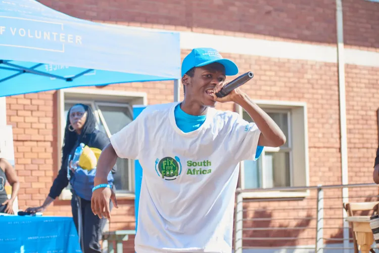 A young man wearing a Fix my Food t-shirt and UNICEF volunteer cap, speaks on a mictrophone
