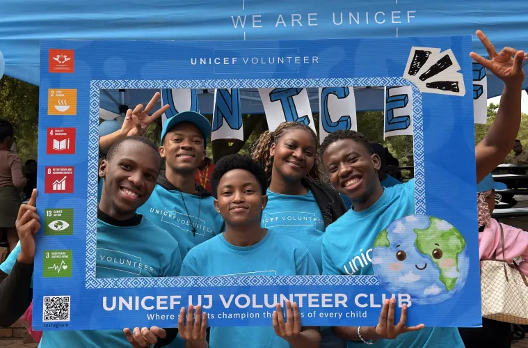 A group of young people wearing blue UNICEF Volunteer t-shirts smile broadly while posing for a photo.