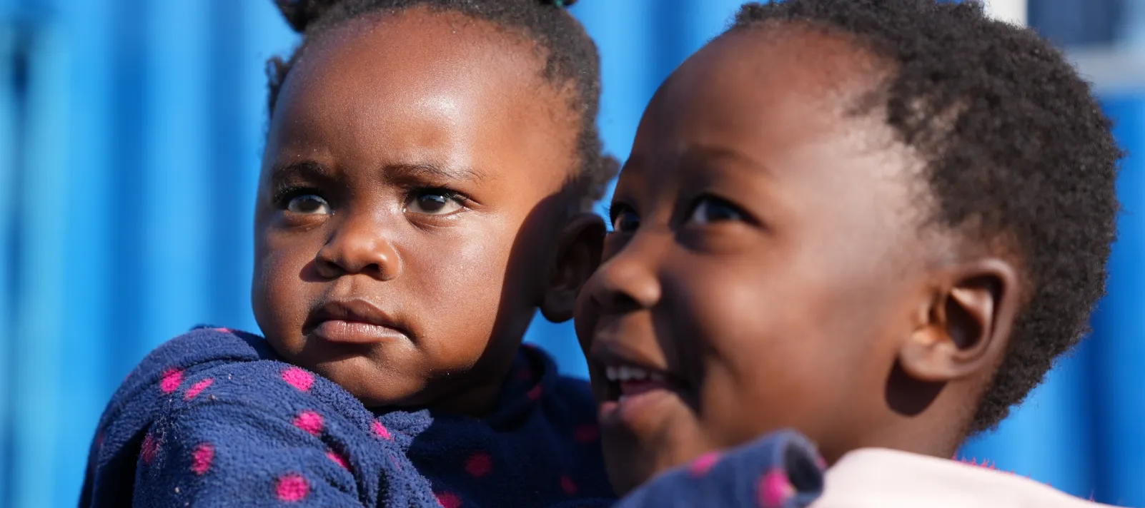 A little girl holds on to a smiling girl that is a little bit older.