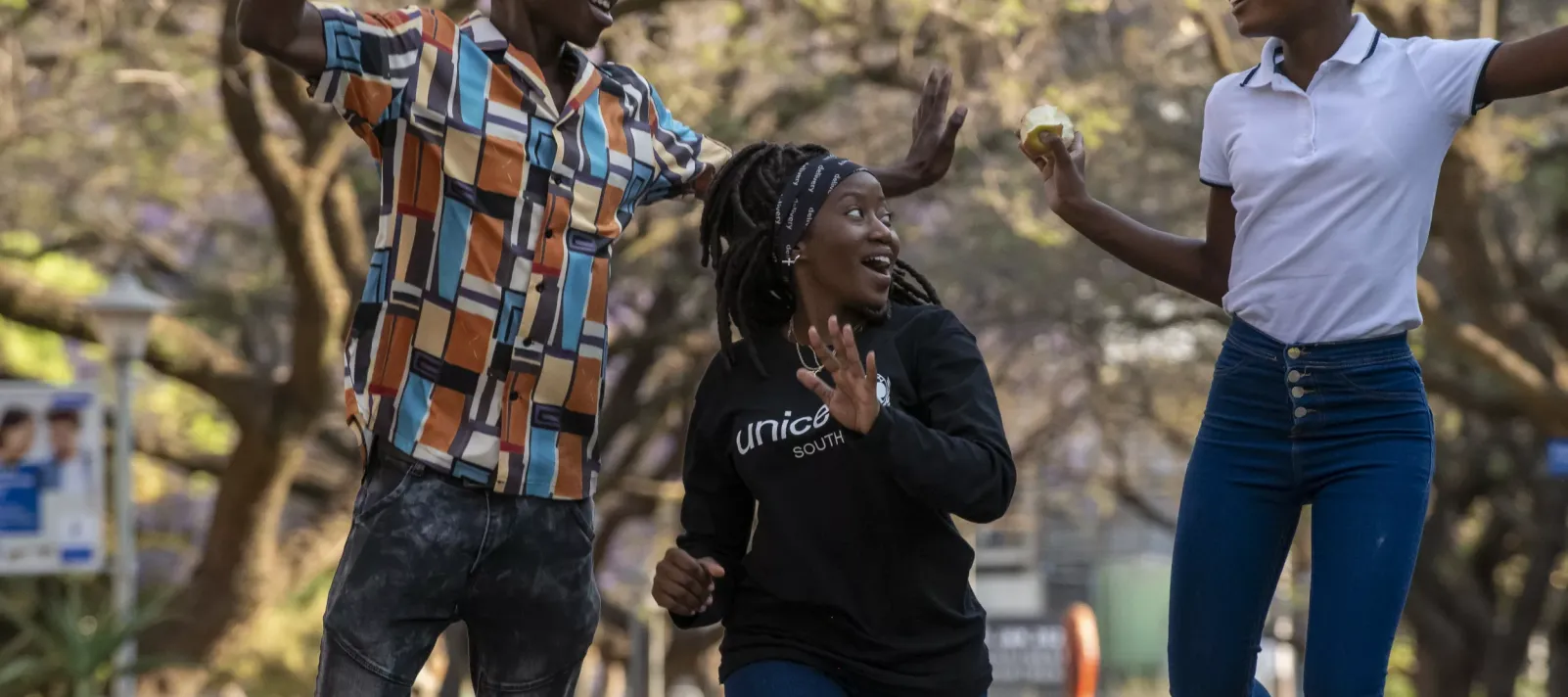 A male and two female UNICEF volunteers jump in the air with joy