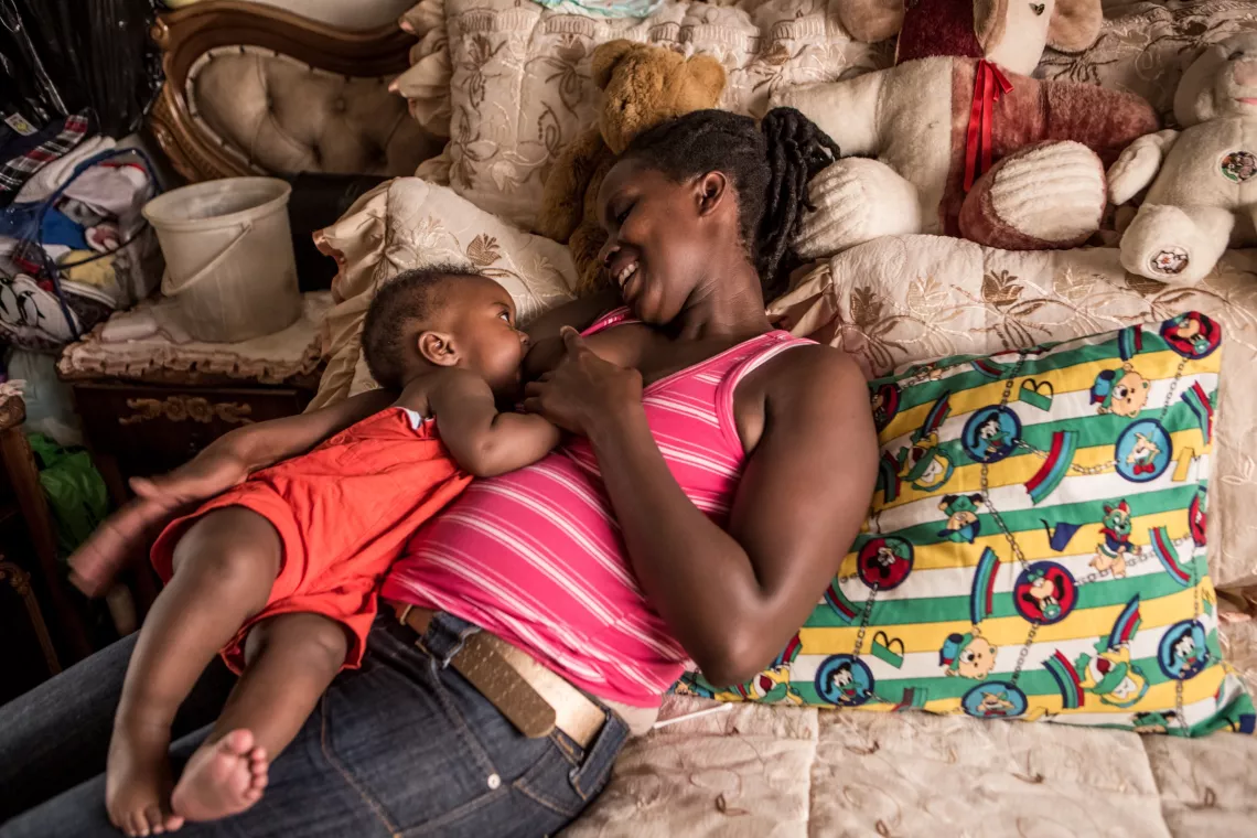 A woman lay on a bed with her infant baby son next to her breastfeeding.