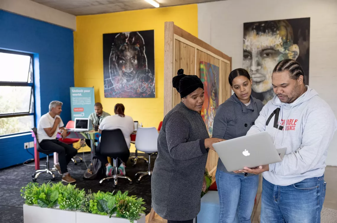 A man shows something to two women on his laptop.