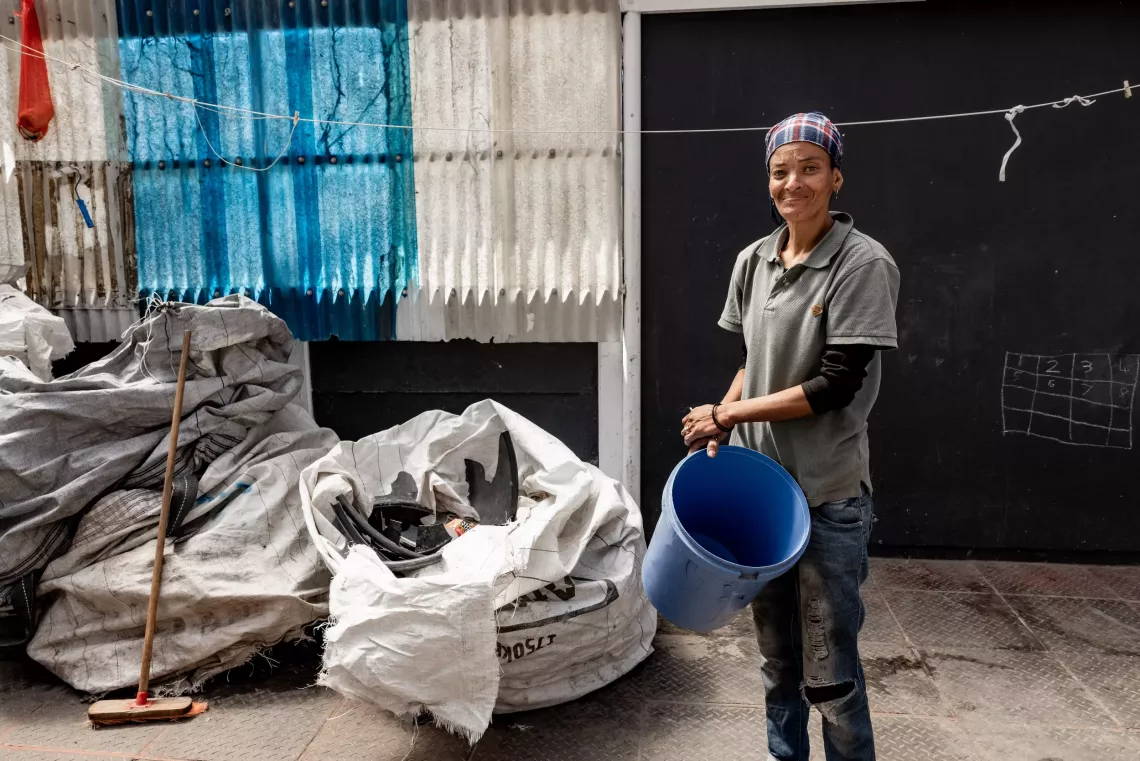 A woman holds a plastic bucket outside a waste drop-off point.