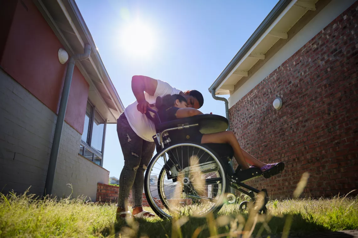 A mother bends down to speak to hear daughter who is in a wheelchair.