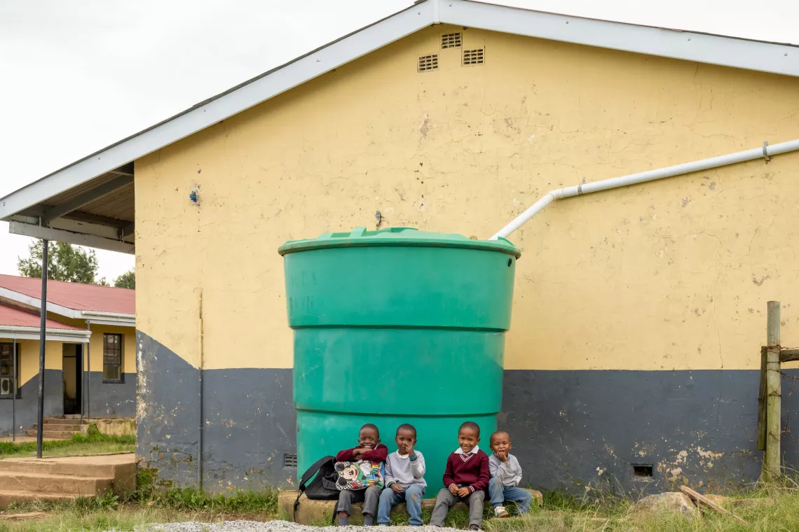 Four little ones from Mbambisa Primary School sit in front of a newly-installed water tank at their school.