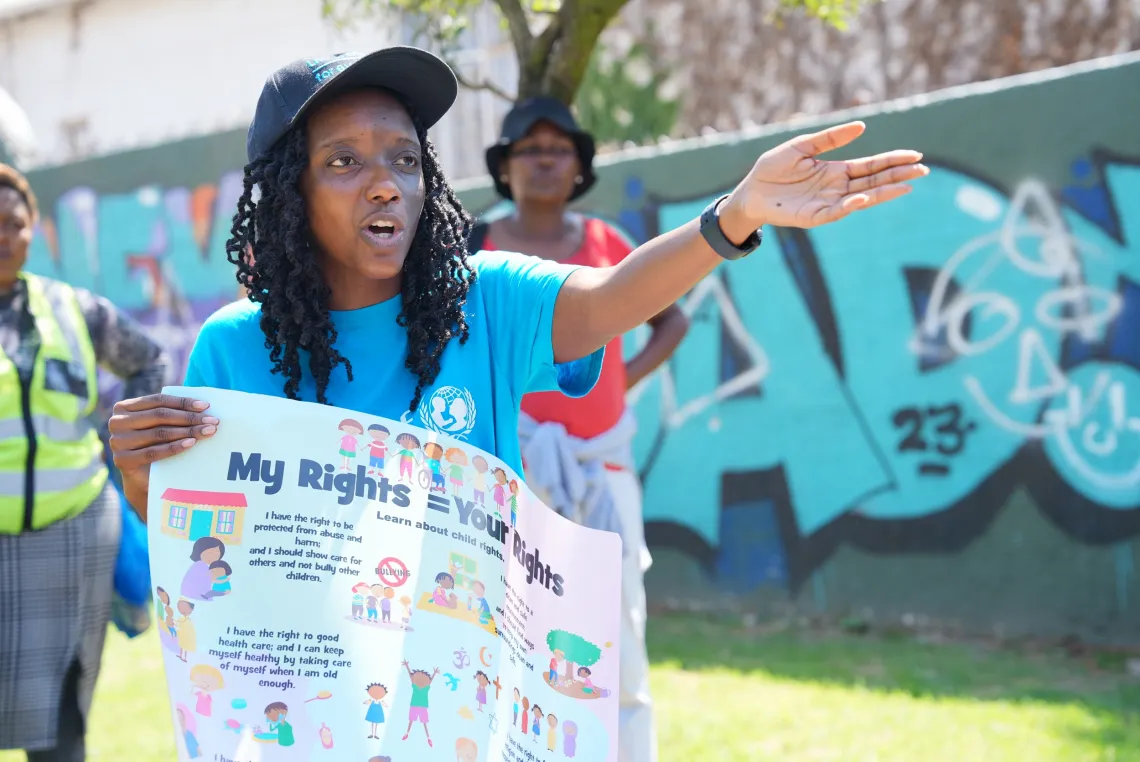 A young woman wearing a blue UNICEF Volunteer t-shirt carries a poster on child rights.