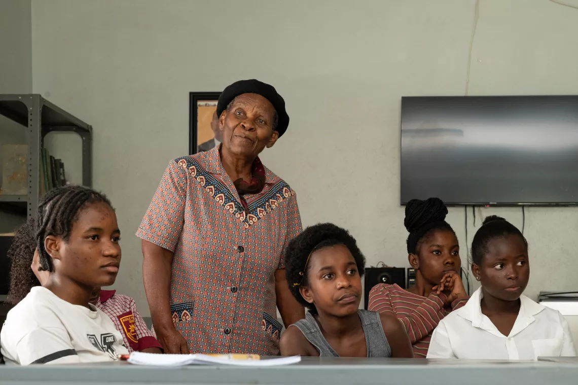 Young girls sitting at a table with an older woman looking on.