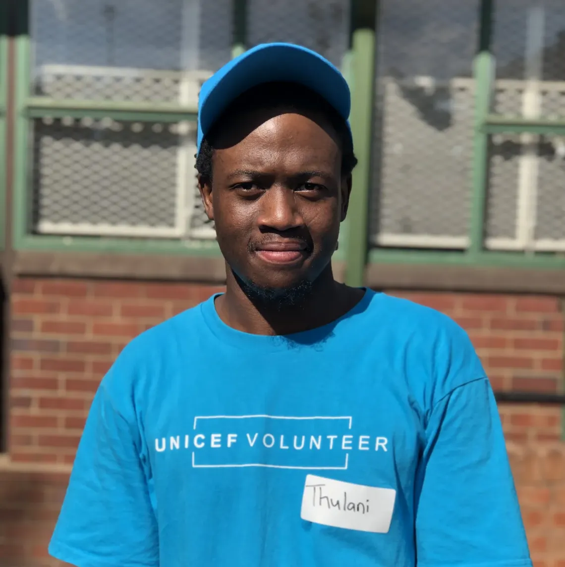 Portrait of a UNICEF Volunteer - Thulani Khumanlo wearing a blue UNICEF volunteer t-shirt and cap.