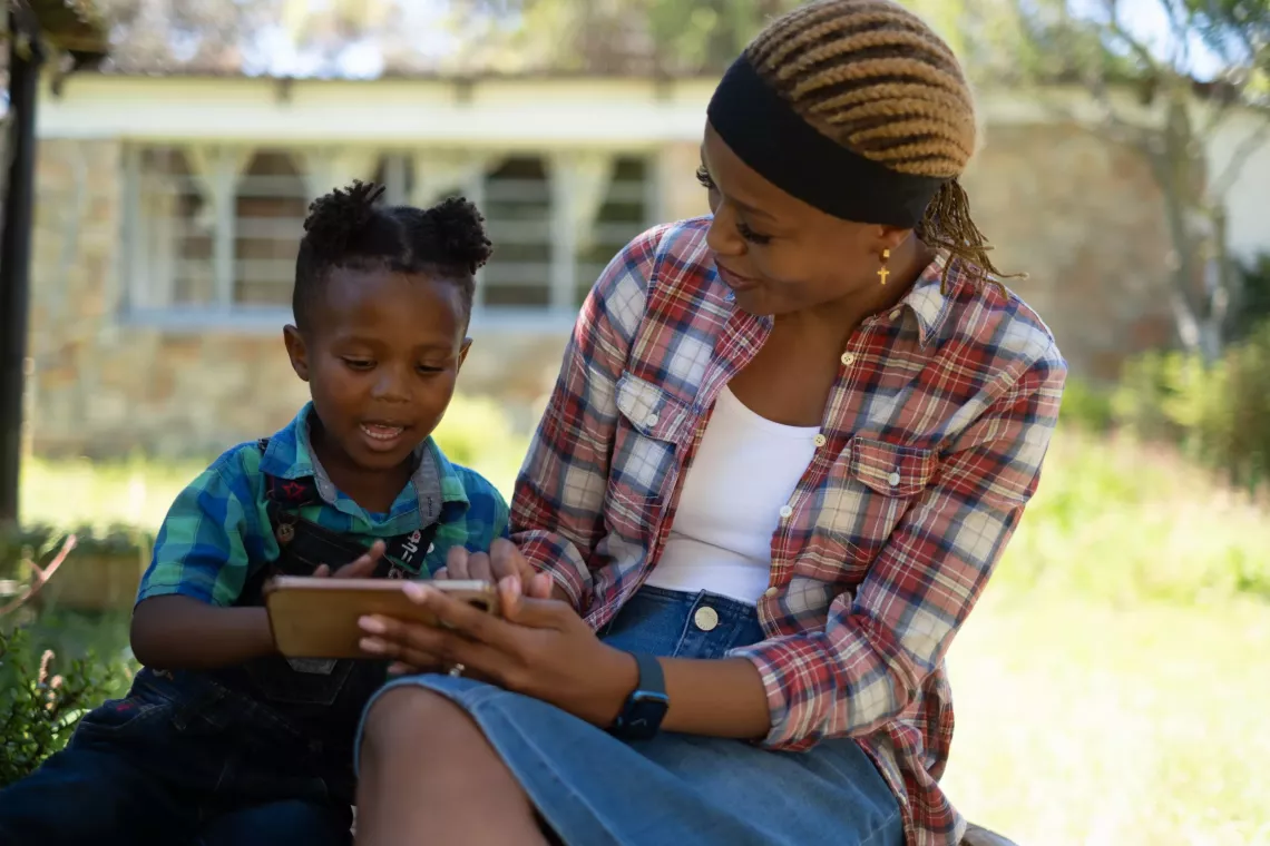 A woman and her daughter sit together looking at content on a mobile phone.