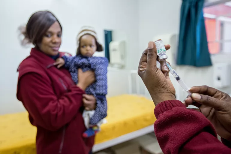 mother holding young child while nurse prepares a vaccine